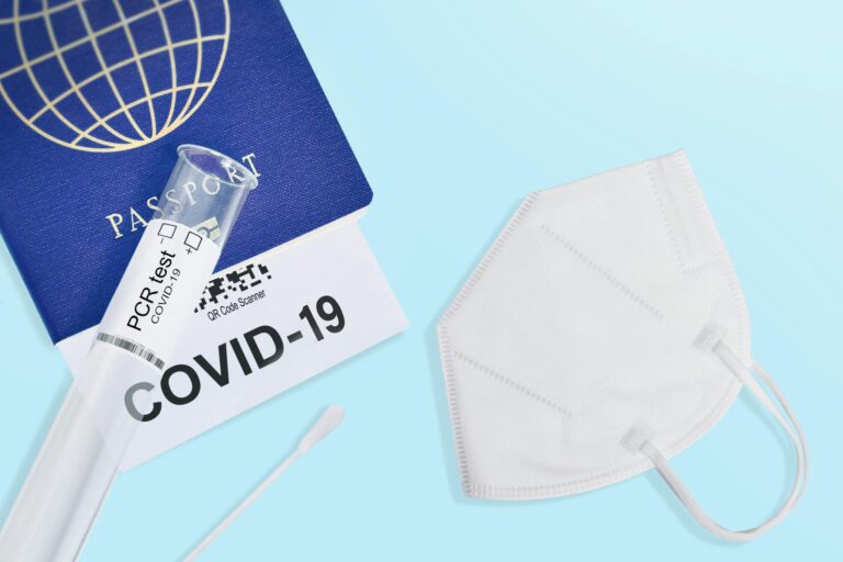 A passport, COVID-19 test, and mask against a blue background symbolizing travel safety during the pandemic.